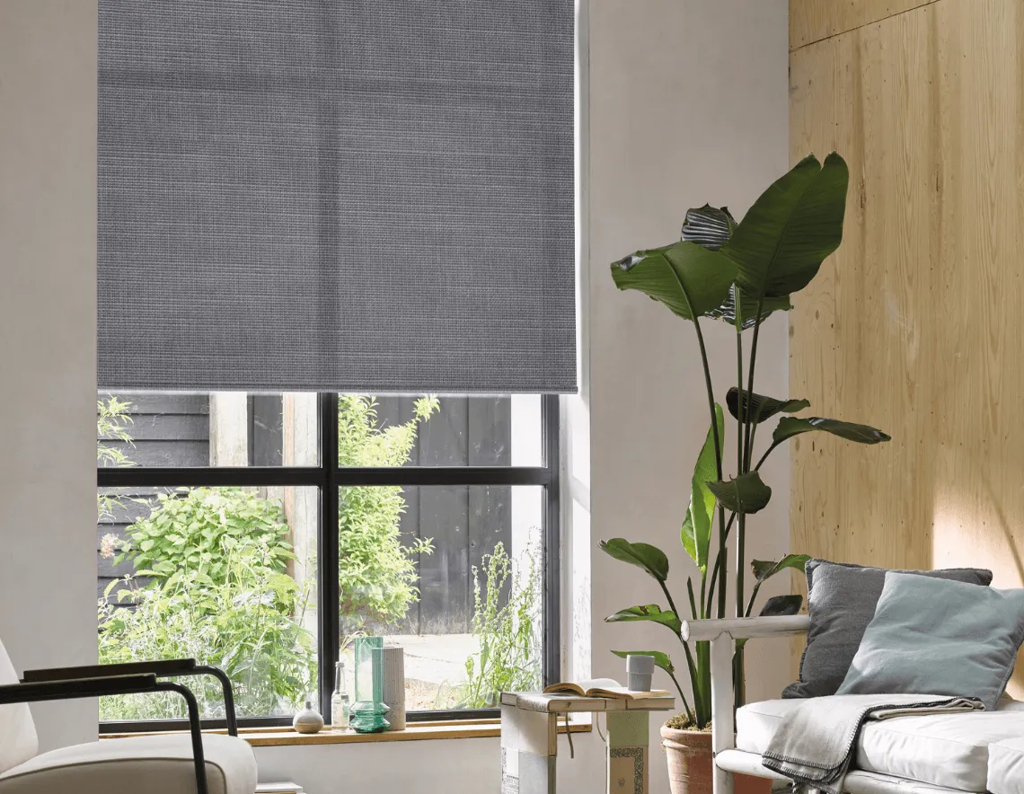 Cortinas Roller gris translucidas, en tela decorativa, en un living con muebles de madera y plantas.